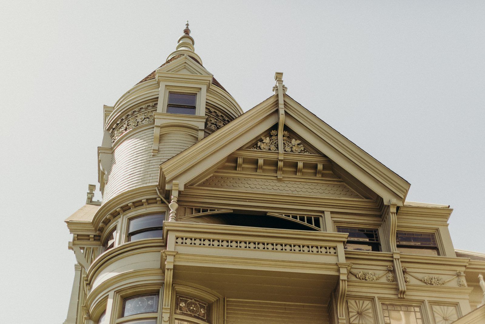 A Victorian house seen from the pavement below: a round tower with a pointed roof, a carved gable and a balcony, against a pale sky.