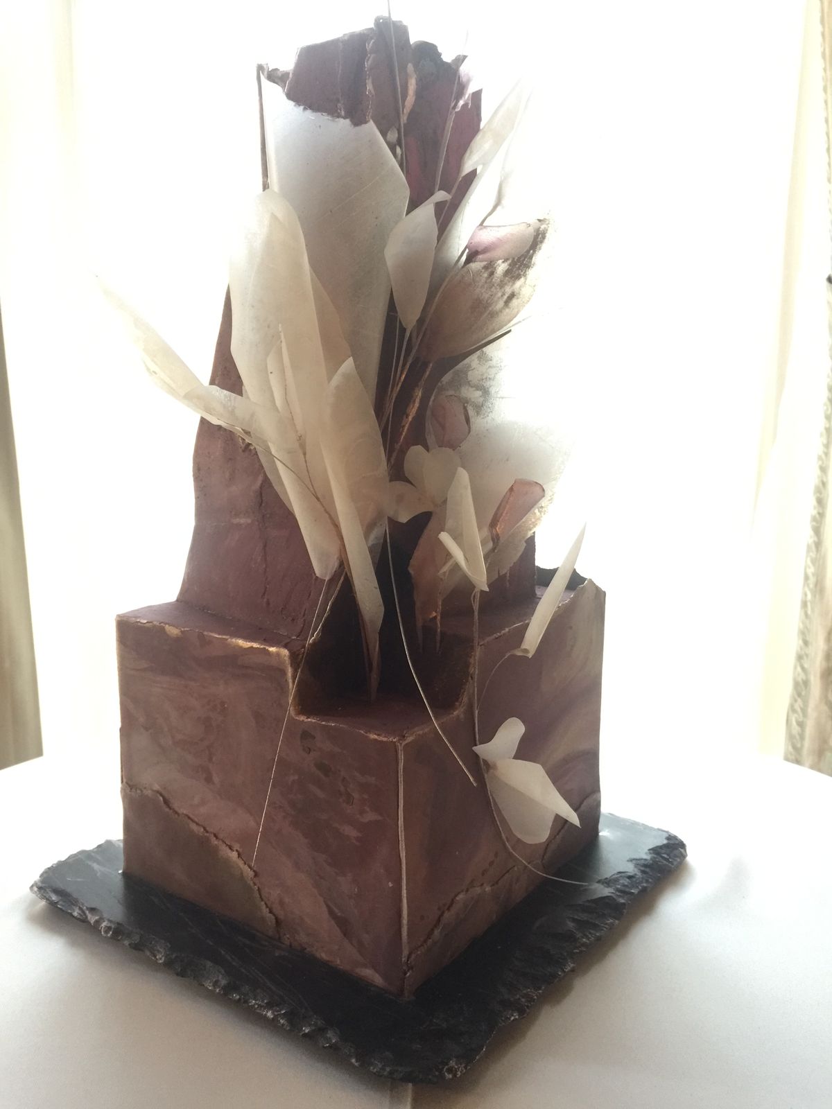 The same cake from the front, the marbled block and the tall fin with its cluster of translucent petals and fine wires.