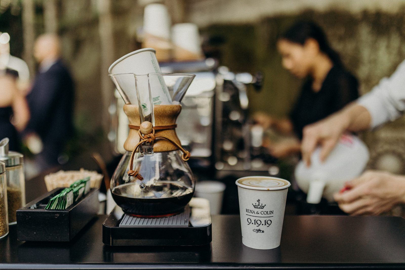 The Hedge coffee bar in the courtyard: a Chemex pour-over coffee maker, a barista pouring milk behind it, and a paper cup stamped with a crown, Rena & Colin and the date 9.19.19.